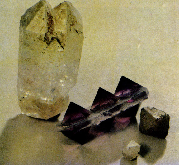 Фото II. Кварцевый двойник, в котором гексагональная призма неожиданно заостряется двумя пирамидками. Рядом - кристаллы аметиста в виде гексагональных пирамид (выращены в автоклаве) и природные кристаллы кварца в виде дипирамид (найдены в Южной Грузии в порфировой жиле месторождения Самшвишде)